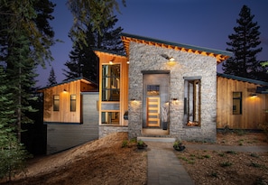Een modern huis met een gevel van natuursteen, houten buitenkant en een goed verlichte entree.
