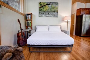 Une chambre à coucher avec un lit, une guitare, une bibliothèque, un tableau, une lampe et un réfrigérateur.