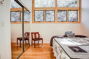 A bedroom with a large window, a bed with a patterned bedspread, two chairs, and a mirror.