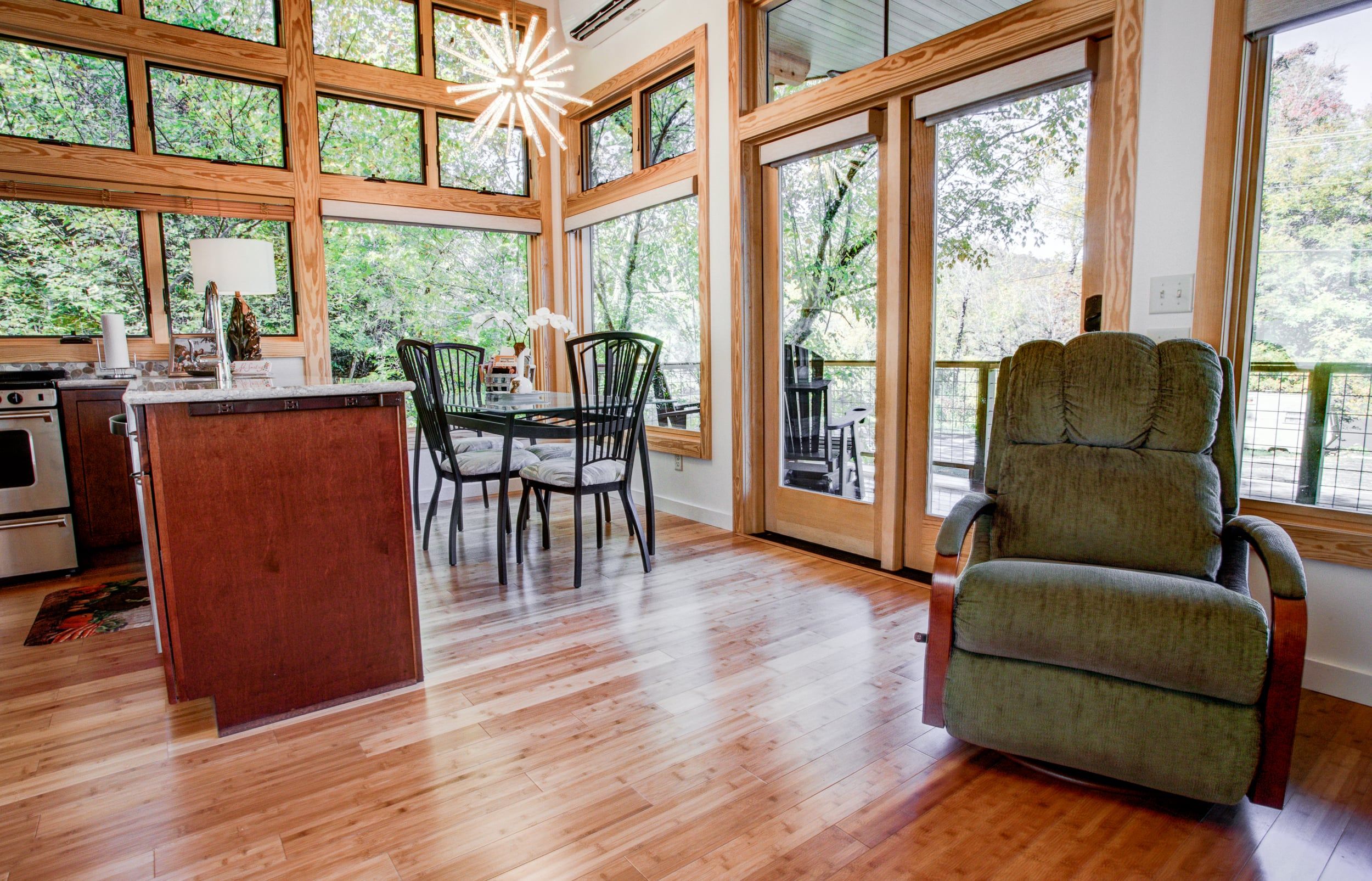 Una cocina amplia con una isla de madera, un comedor con sillas y ventanas grandes que ofrecen vistas al exterior.
