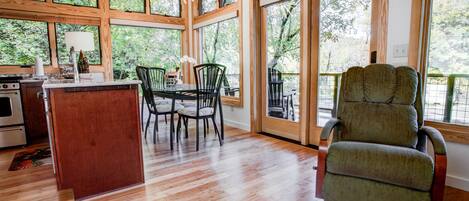 Una cocina amplia con una isla de madera, un comedor con sillas y ventanas grandes que ofrecen vistas al exterior.