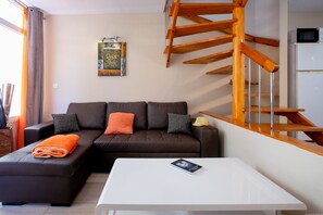 Una sala moderna con un sofá seccional marrón, una mesa de centro blanca y una escalera de madera.