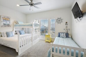 Habitación infantil con literas, ventilador de techo, televisión y decoración náutica.