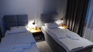 A hotel room with two single beds, each with a bedside table, lamp, and a small table between the beds. - ApartHotel I SORAU (Zary)