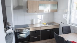 A modern kitchen with a built-in oven, a sink, and a dining area with a table and chairs. - Ferienwohnung Anke-Apartement 5a (Heinsberg)