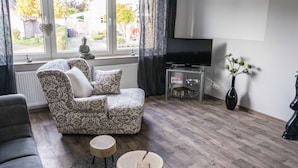 A living room with a patterned sofa, a small wooden table, a television, and a vase with flowers. - Ferienwohnung Anke-Apartement 5a (Heinsberg)
