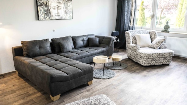 A modern living room with a sectional sofa, a patterned armchair, and a small side table. - Ferienwohnung Anke-Apartement 5a (Heinsberg)