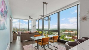 A modern living room with a dining area, large windows, and a city view. - Endless Sunset Retreat | Arras Vacation Rentals (Asheville)