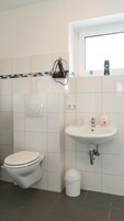 Un baño con inodoro, lavamanos, un cubo de basura y una ventana.