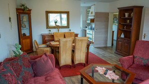 A living room with a red sofa, a glass coffee table, a dining table with chairs, a wooden cabinet, and a mirror on the wall. - Ferienwohnung Anke-Apartement 5b (Heinsberg)