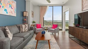 Una sala de estar moderna con un sofá gris, dos sillones, una mesa de centro, un televisor y un ventilador de techo.