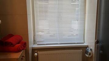 A bathroom with a window, a radiator, a toilet, and a shower area.