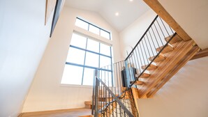 Een modern interieur met een houten trap, grote ramen en een hoge plafond.