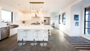 Een moderne keuken met een groot eiland, roestvrijstalen apparatuur en hangende lampen.