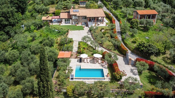 Une grande maison avec une piscine, entourée d’une végétation luxuriante et située dans un paysage vallonné.