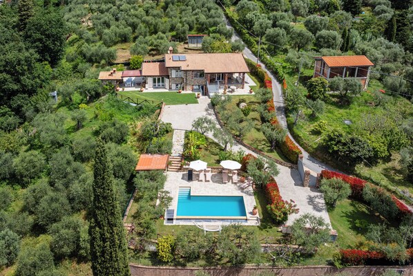 A large house with a swimming pool, surrounded by lush greenery and a hilly landscape.