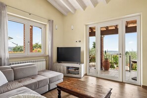 Un salon comprenant un canapé, un téléviseur posé sur un meuble, une table basse en bois et une porte-fenêtre coulissante donnant sur une terrasse extérieure.
