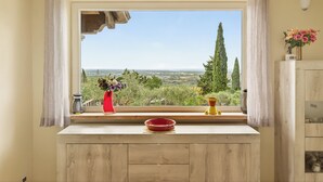 Une cuisine avec une fenêtre donnant sur l’extérieur, un meuble en bois, un saladier rouge et un vase rempli de fleurs.
