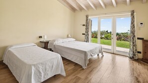 Une chambre avec deux lits, un plafond en bois, une porte-fenêtre coulissante donnant sur l’extérieur, une petite table de chevet avec une lampe et un thermostat fixé au mur.