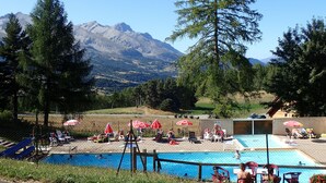 Piscina con vistas a montañas al fondo, rodeada de árboles y zonas de estar al aire libre.
