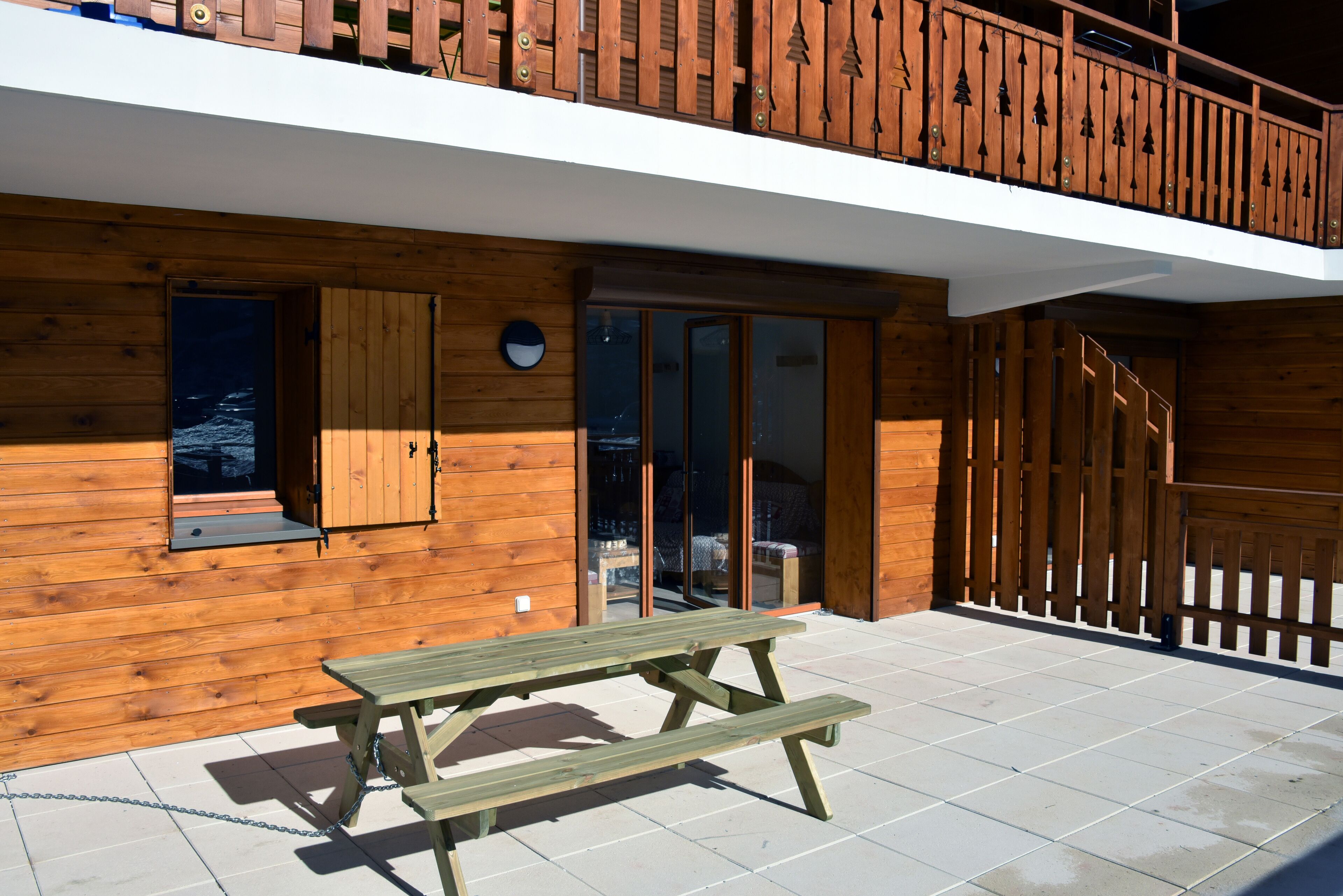 A wooden cabin with a balcony, a wooden door, and a picnic table.
