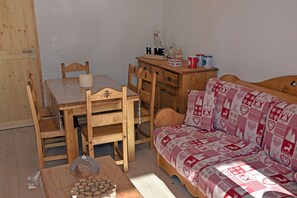 A cozy room with a wooden dining table, chairs, a wooden sofa with a patterned cover, and a wooden dresser with decorative items.