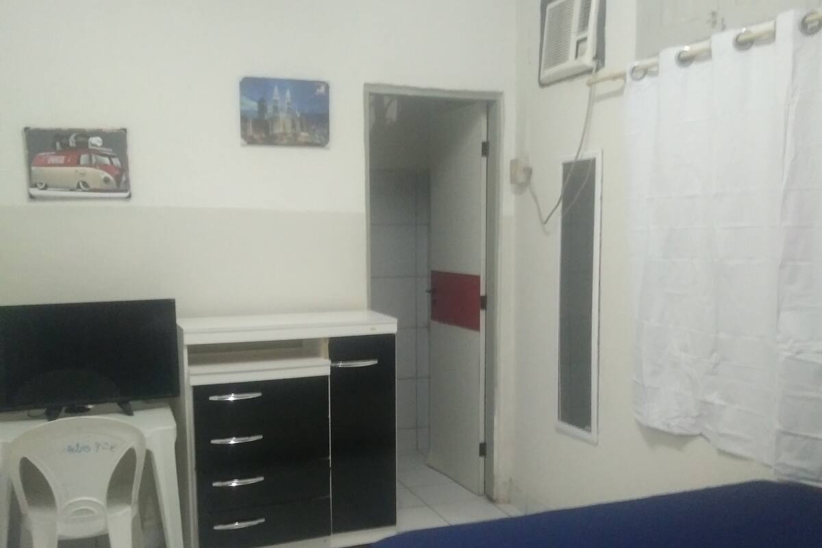 A bedroom with a bed, a desk, a chair, a wardrobe, a television, and a door leading to a bathroom.