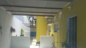 A covered outdoor area with a tiled floor, yellow walls, and white pillars. - Prad Residence (Recife)