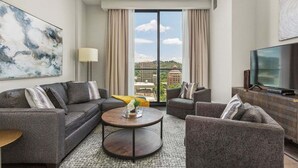 Ein modernes Hotelzimmer mit einer Sofagarnitur, einem Couchtisch, einem Fernseher und einem großen Fenster mit Vorhängen.