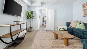 Un salon moderne avec un téléviseur à écran plat, une table basse en bois, un canapé et un tapis à motifs.