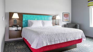 A hotel room with a bed, two bedside lamps, a map on the headboard, a framed picture on the wall, and a window with a striped curtain.
