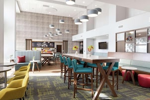 Um lobby de hotel moderno com área de bar, assentos e uma tela grande.