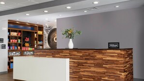 Ein Hotelrezeptionstresen mit Holzdesign, einer weißen Theke und einem Schild, das angibt, dass es sich um eine Hilton Honors Location handelt.