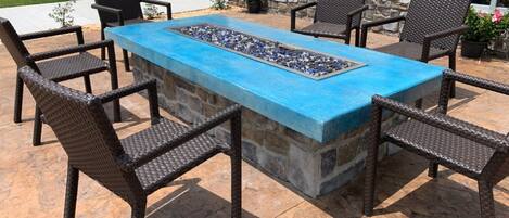 An outdoor patio with a rectangular table, six wicker chairs, and a stone wall backdrop.
