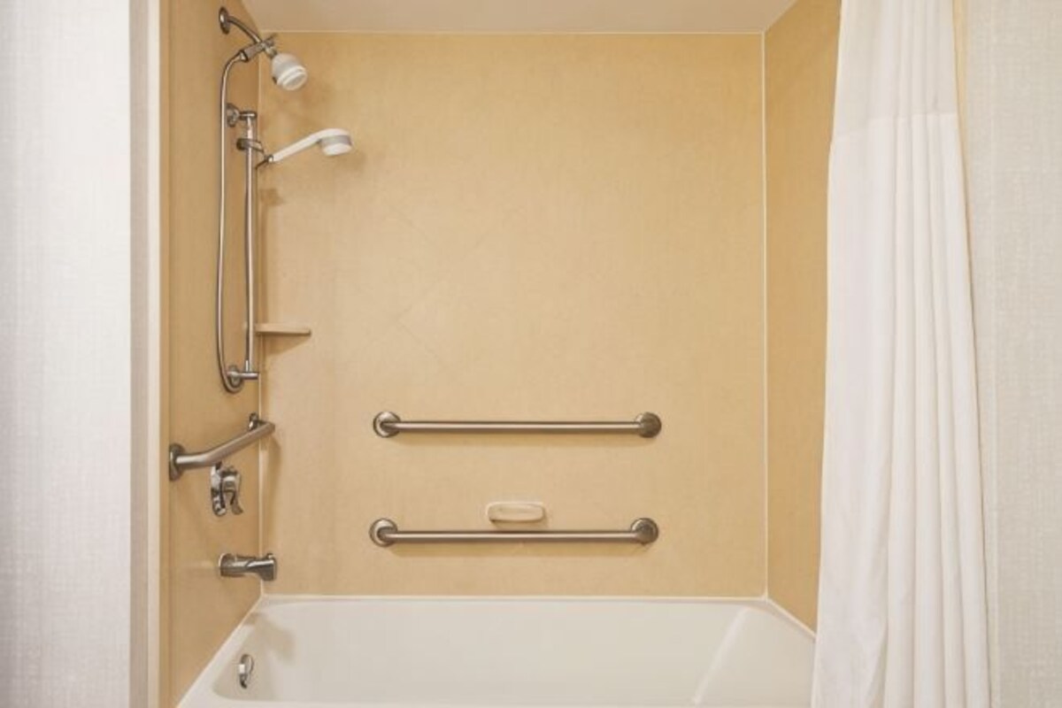 A bathroom with a bathtub, grab bars, a showerhead, and a curtain.