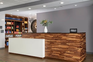 Uma receção de hotel com design em madeira, balcão branco e placa indicando ser um local Hilton Honors.