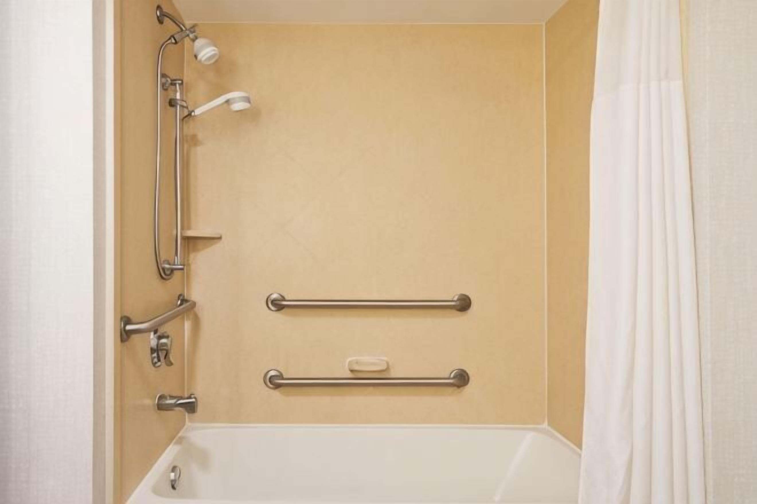 A bathroom with a bathtub, grab bars, a showerhead, and a curtain.