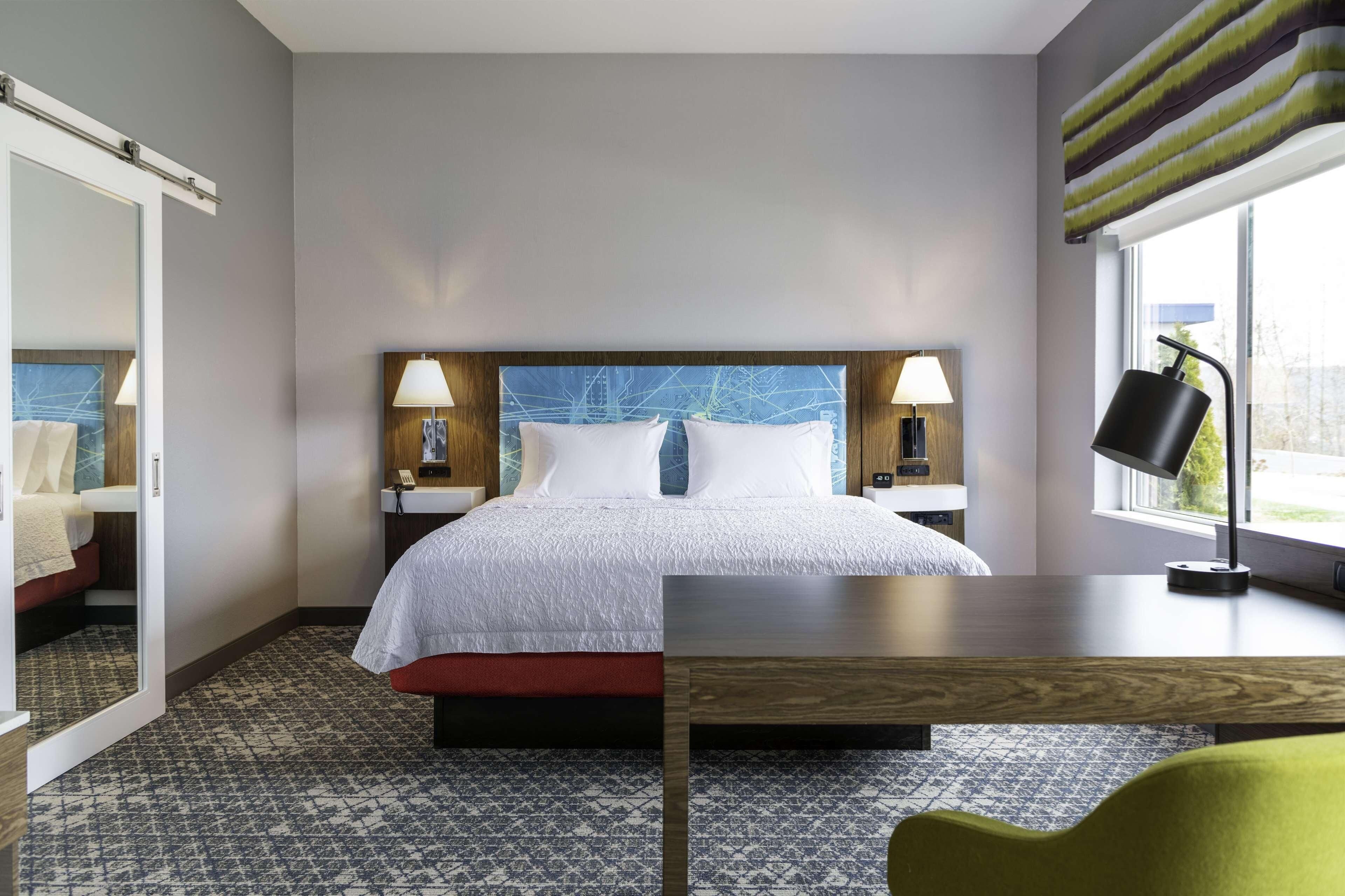 Una habitación de hotel con una cama grande, dos mesitas de noche con lámparas, un escritorio de madera y una silla.
