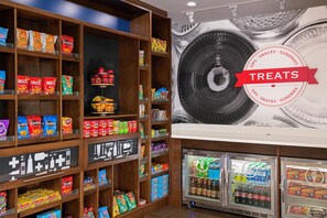 A snack display with various chips and snacks, a refrigerated section with beverages, and a wall with a large tire graphic. - Hampton Inn & Suites Pittsburgh New Stanton (New Stanton)