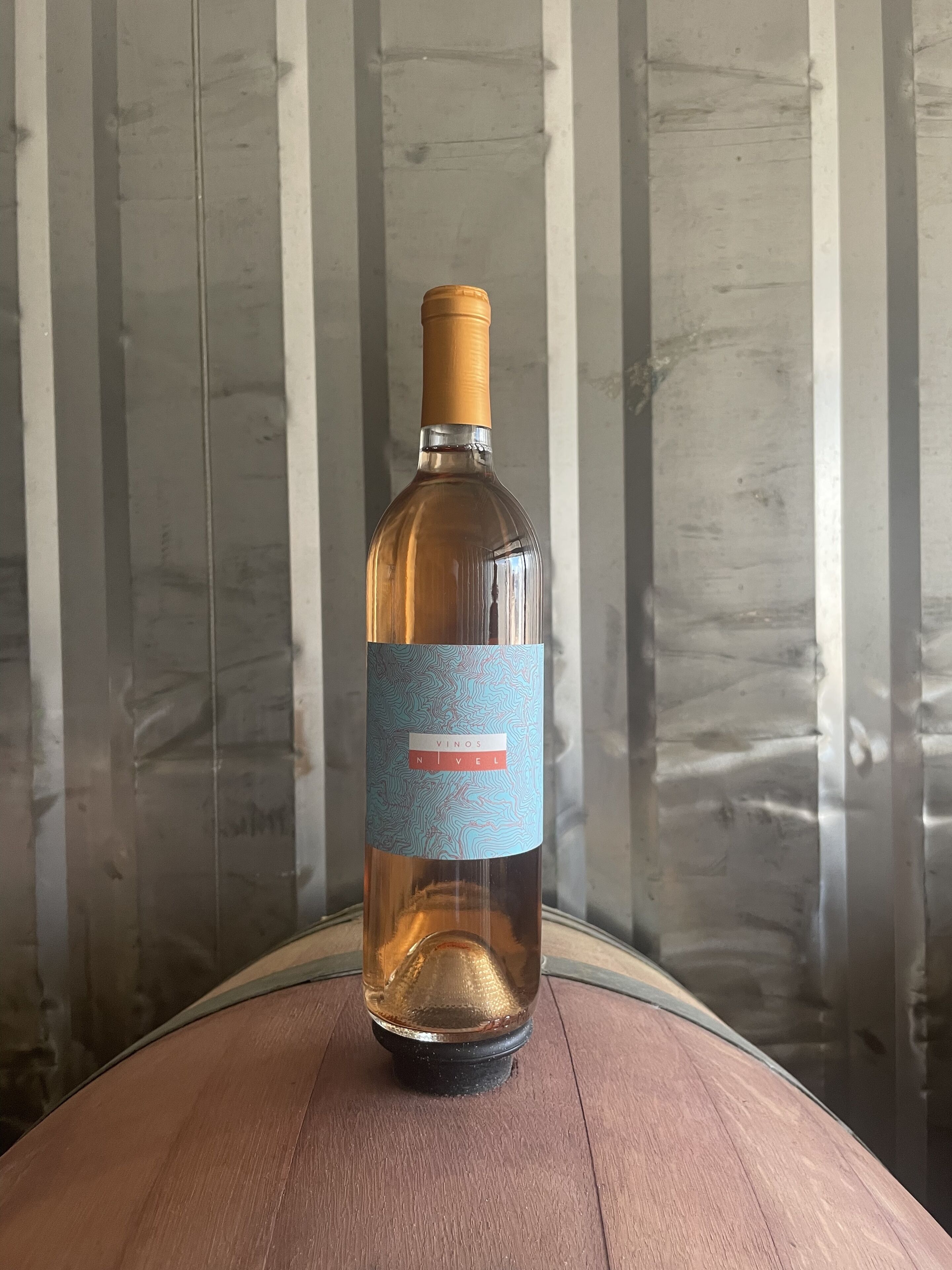 Una botella de vino sobre una mesa de madera, con una pared texturizada al fondo.