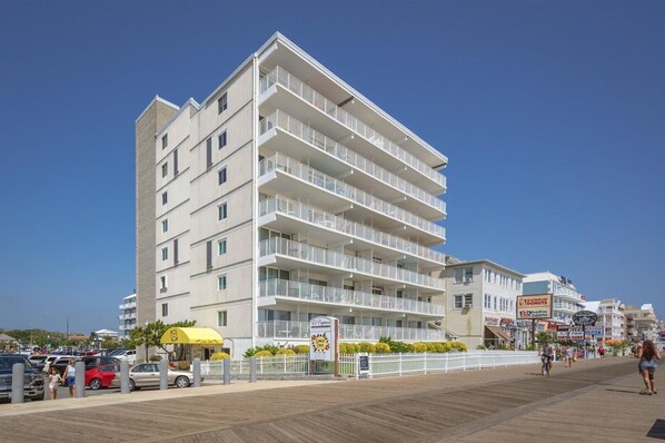 Un hôtel à plusieurs étages doté de balcons, une promenade en bord de mer devant l’établissement et divers commerces.