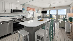 A modern kitchen with white cabinets, stainless steel appliances, and a central island with bar stools. - On the Boardwalk, 1st floor end unit, Ocean front, 4th Street, Ocean City, MD (Ocean City)