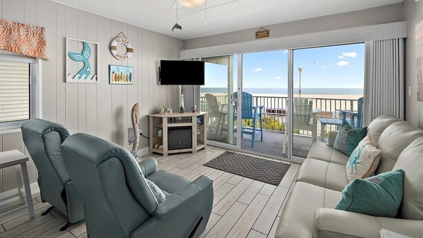 A spacious living room with a large TV, comfortable seating, and a balcony with a view of the beach. - On the Boardwalk, 1st floor end unit, Ocean front, 4th Street, Ocean City, MD (Ocean City)