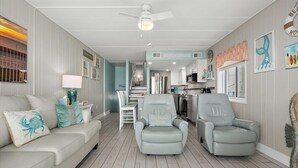A living room with a sofa, two armchairs, a coffee table, and a dining area with a table and chairs. There is a kitchen in the background with a microwave and a refrigerator. - On the Boardwalk, 1st floor end unit, Ocean front, 4th Street, Ocean City, MD (Ocean City)
