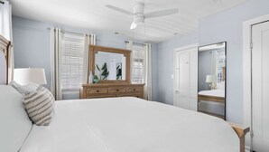 A bedroom with a large bed, a wooden dresser, a ceiling fan, and a mirror. - Historic Charleston Style House (Charleston)