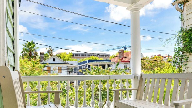 A covered porch with two wooden benches and a railing, overlooking a residential area with houses and greenery. - Historic Charleston Style House (Charleston)