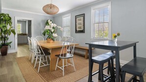 A dining area with a wooden table, white chairs, a bench, and a black table. There are potted plants and a hanging light fixture. - Historic Charleston Style House (Charleston)