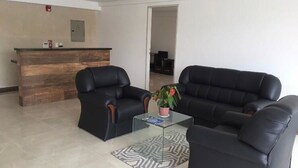 A modern living room with two black leather sofas, a glass coffee table, and a patterned rug. A reception desk with a wooden finish is visible in the background. - Edificio Mirage - Zona Vip de Asunción (Asunción)