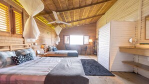Una habitación acogedora con paredes de madera y un ventilador de techo, que incluye dos camas con distintos estilos de ropa de cama y una pequeña zona de escritorio.