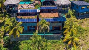 Un resort con varias construcciones, algunas con techos de paja y paneles solares, rodeado de exuberante vegetación y palmeras.